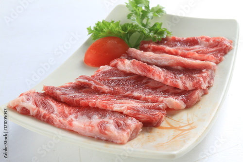Sliced fresh raw beef on white plate with tomato and herbs