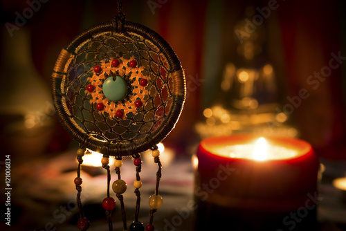 Vintage style image of dreamcatcher and candle light with blurred Buddha statue on the background.