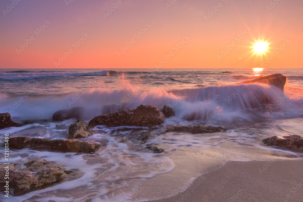Obraz premium Sea sunrise. Beach and rocks with slow shutter and waves flowing out.