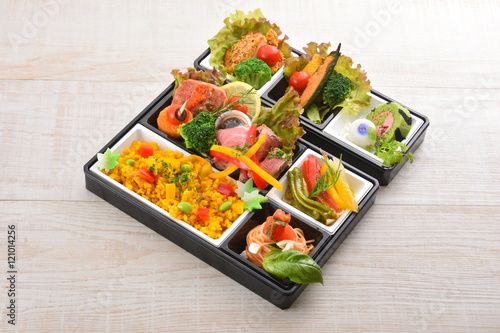 Bento meal of rice, salmon, broccoli, lettuce and noodle on wood