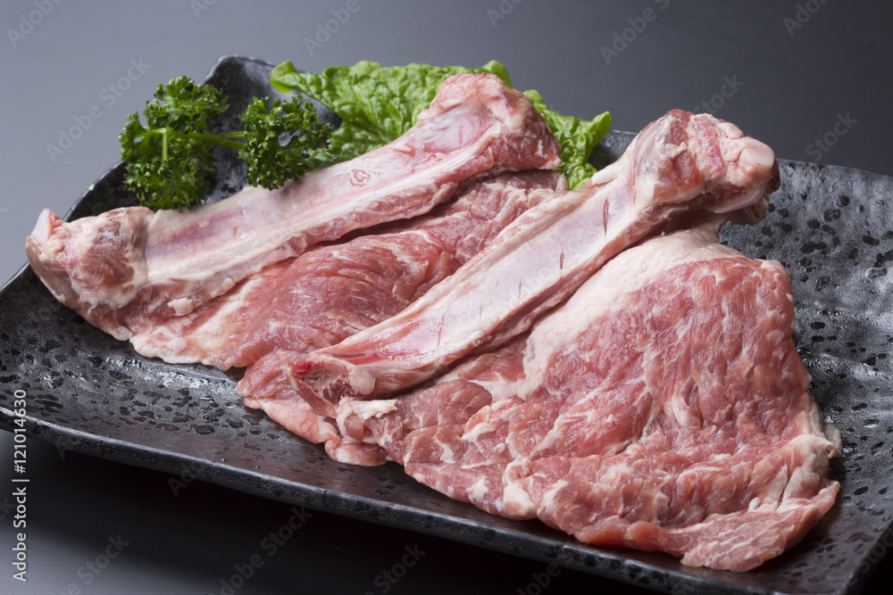 Fresh bone in pork ribs with lettuce on black dish