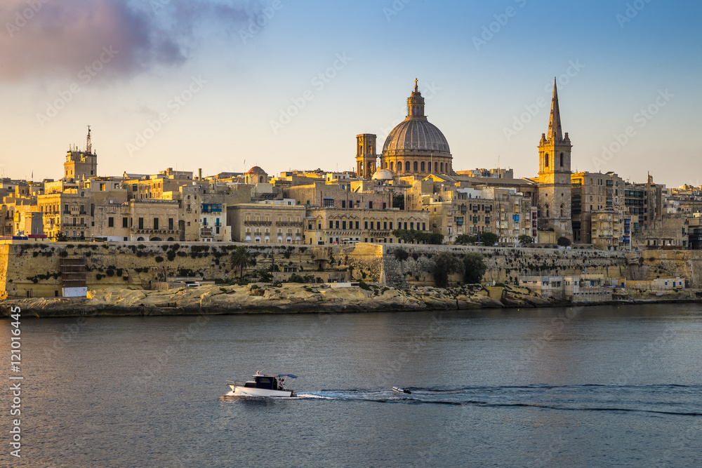 Valletta, Malta - St.Paul's Cathedral and the ancient city of Valletta with motorboat at sunrise