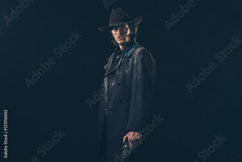Menacing vintage 1900 cowboy standing with revolver. Studio shot