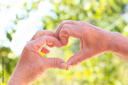 Hands of old senior showing heart