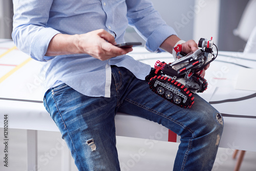 Male hands holding little robot and cell-phone