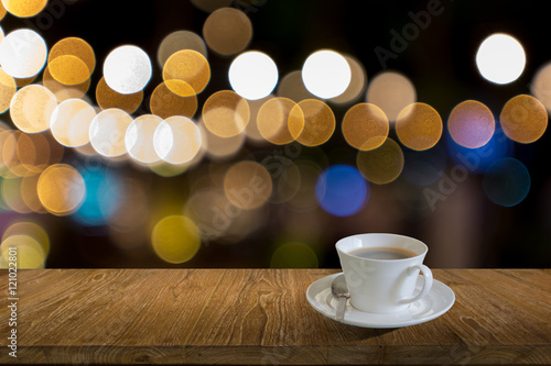 image of white cup of coffee and wooden table in front of abstract blurred background of lights, image for add text
