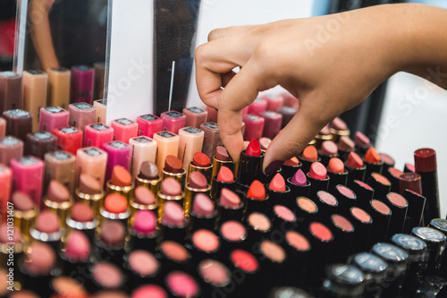 Woman takes a lipstick. Store, shopping room, makeup salon. The multi-colored lipstick set.