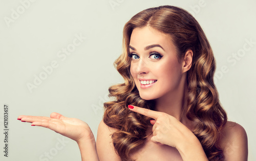 Woman surprise showing product .Beautiful girl with curly hair pointing to the side . Presenting your product. Expressive facial expressions 