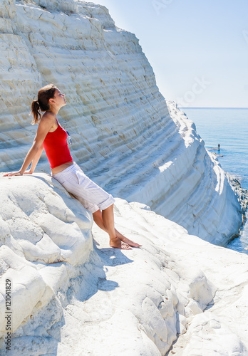 A girl sits on a slope of white cliff called "Scala dei Turchi"