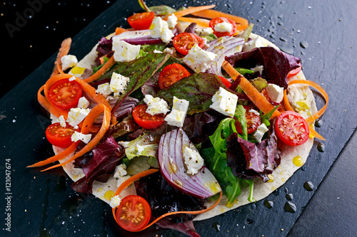 Vegetarian tortillas taco wrap with red onion, sweet cherry tomatoes, carrots, ruby chard, rocket and feta chees drizzled olive oil