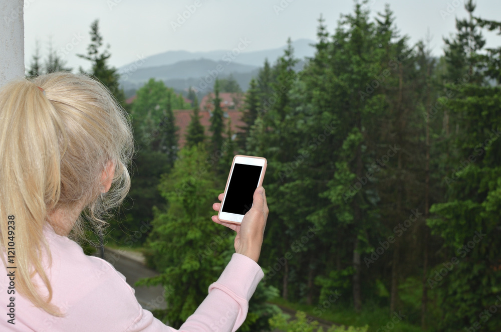 Woman with ponytail looking at landscape and her black cell phone screen suitable for copy text or picture