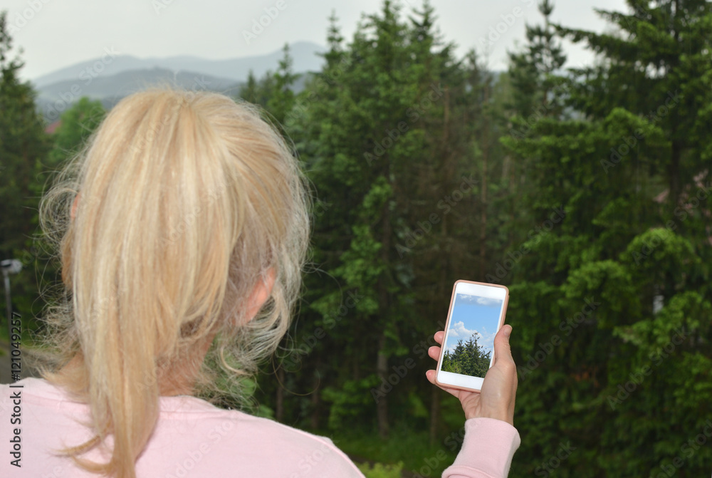 Woman looking at cloudy landscape and her cell phone screen with a picture of the same landscape on nice weath