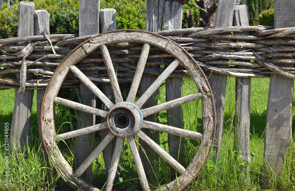 Closeup of an old wheel of a traditional cart leaning on a wooden fence