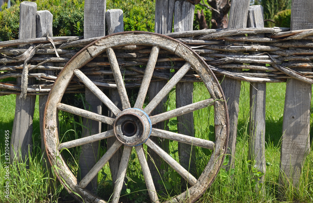 Closeup of an old wheel of a traditional cart leaning on a wooden fence Closeup of an old wheel of a traditional cart leaning on a wooden fence