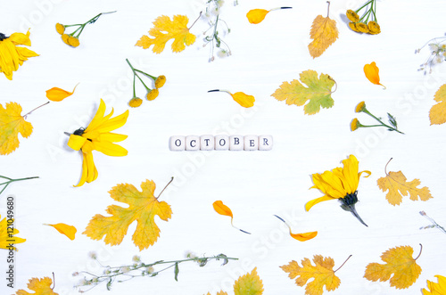 The word october on the background of yellow flowers and leaves