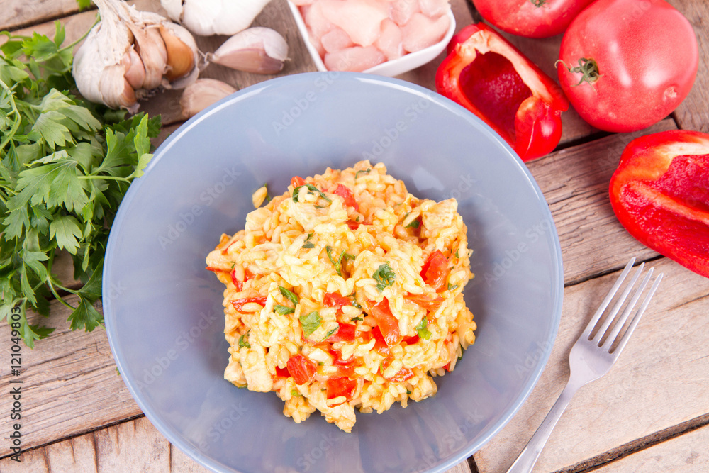 Risotto with chicken, tomatoes, bell pepper, onion, parsley and garlic on a blue plate on a wooden background Risotto with chicken, tomatoes, bell pepper, onion, parsley and garlic on a blue plate on a wooden background