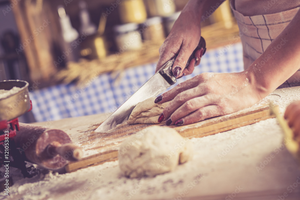 Close up of female baker hands cutting dough and making bread. Retro look.