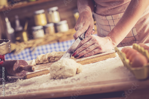 Close up of female baker hands cutting dough and making bread. Retro look.