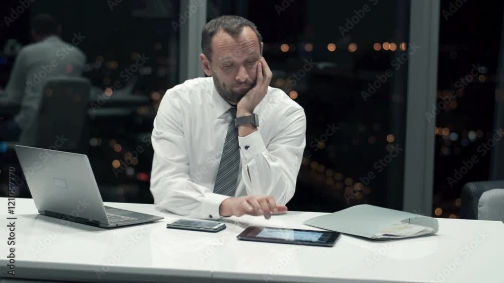 Bored businessman sitting by desk in office at night
Bored businessman sitting by desk in office at night