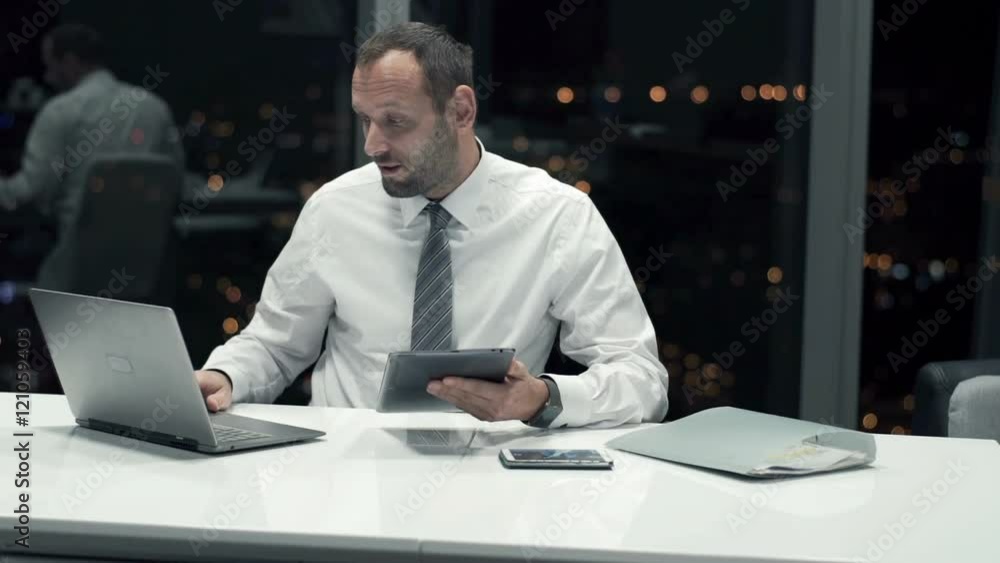 Friendly businessman with tablet and laptop talking good news in office at night
Friendly businessman with tablet and laptop talking good news in office at night
