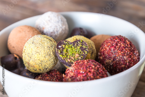 Colorful dessert, raw vegan sweets and organic chocolate in a bowl on a wooden background, close-up.