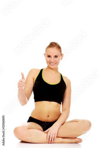 Athletic woman sitting cross legged on the floor and show thumb up