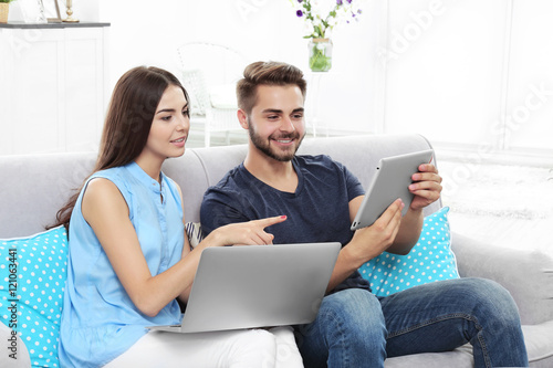 Beautiful young couple using laptop and tablet at home