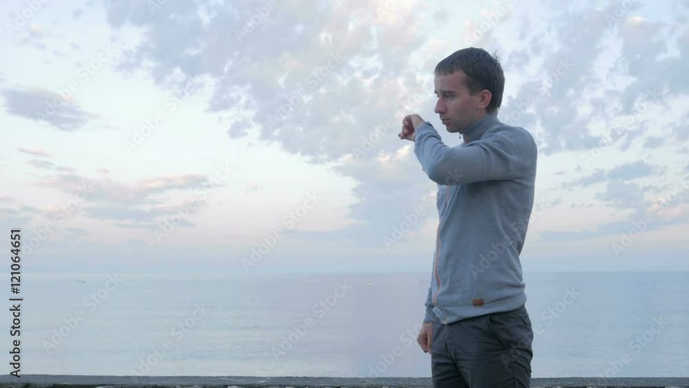 A man walks along the beach and check the messages on the smart watch near the ocean. He is responsible in social networks A man walks along the beach and check the messages on the smart watch near the ocean. He is responsible in social networks