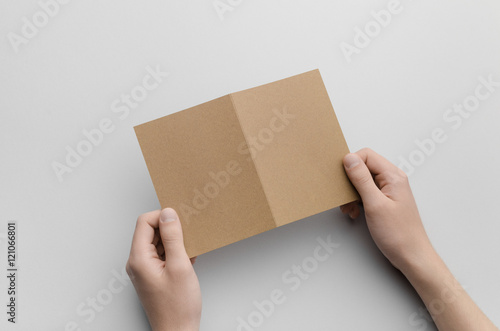 Kraft A6 Bi-Fold / Half-Fold Brochure Mock-Up - Male hands holding a kraft bi-fold on a gray background.