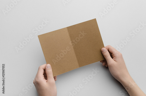 Kraft A6 Bi-Fold / Half-Fold Brochure Mock-Up - Male hands holding a kraft bi-fold on a gray background. © Shablon