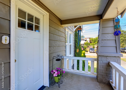 Concrete floor porch of siding house. Flower pot and white entry door.