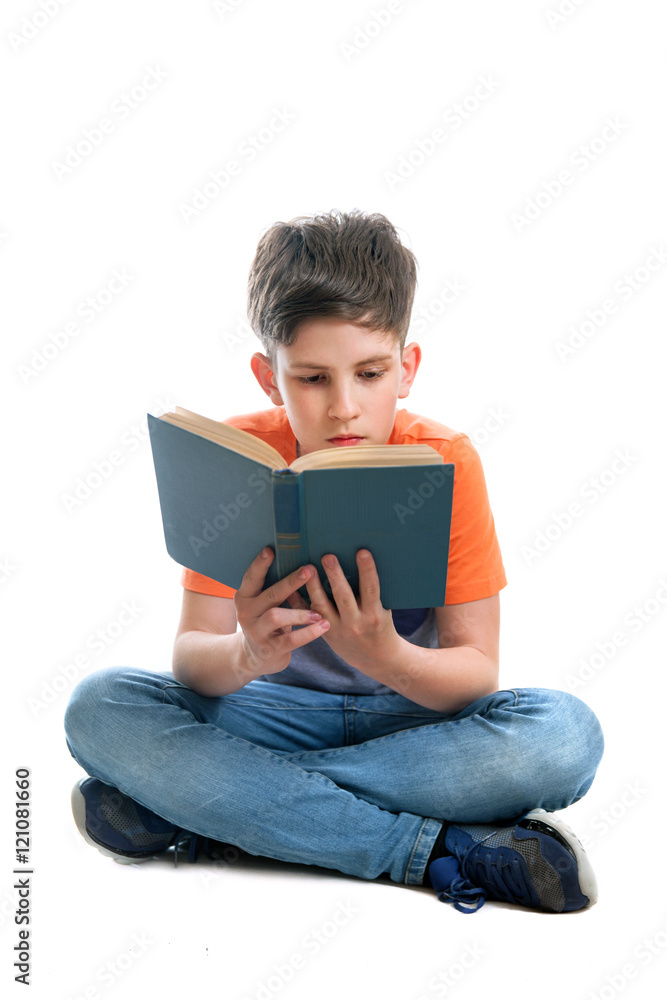 A school-boy is sitting on the floor and reading a book