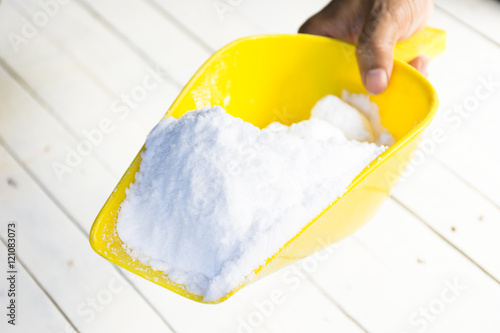 Dextrose in yellow shovel in hand on wooden white table