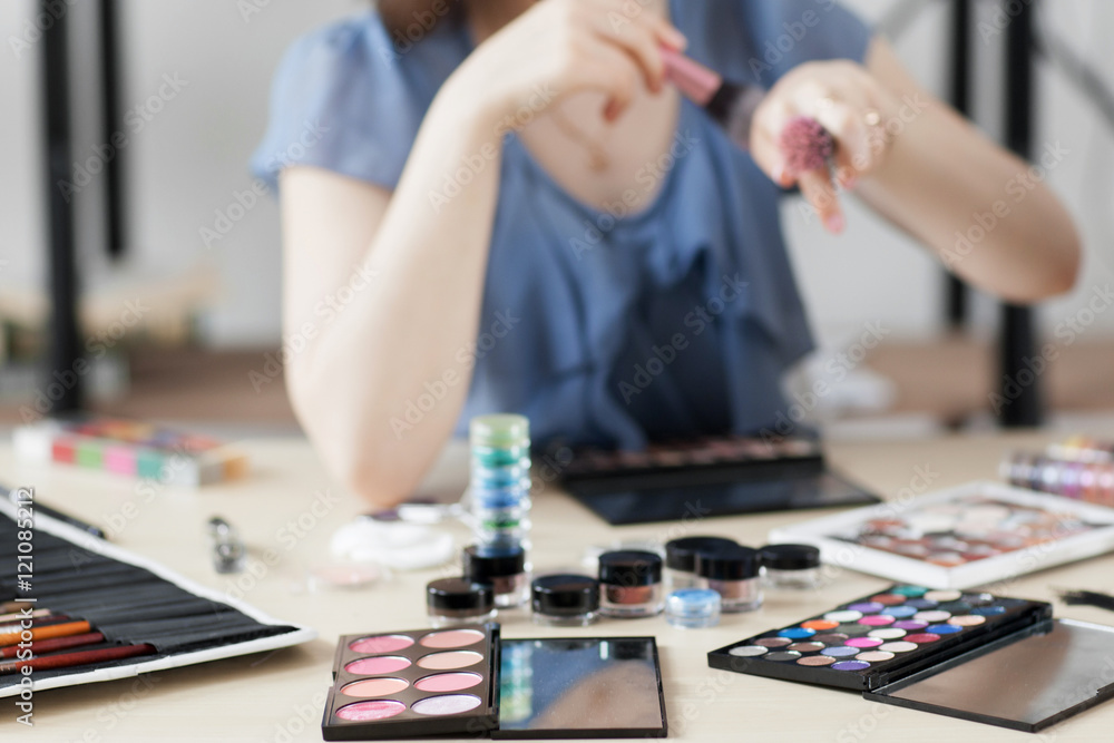 Colorful cosmetics on stylist workplace. Visagiste trying brush on hand. Stylish ladies lifestyle accessories. Variety of makeup tools, palettes and brushes.