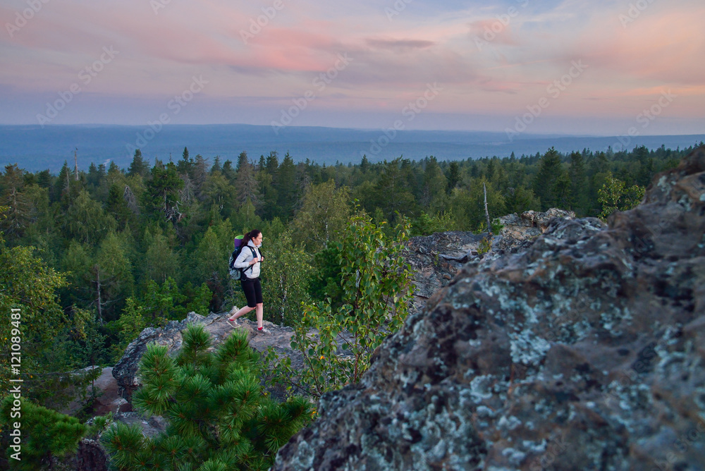 Obraz premium Lady hiker with backpack standing on top of the mountain and enjoying valley view at sunset