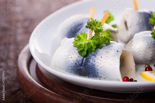 Rollmops (rolled marinated herring) with marinated cucumber, salt, pepper and parsley, closeup