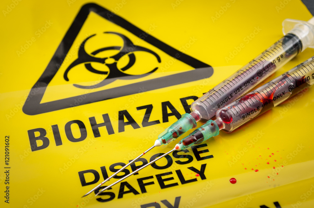 Blood filled medical syringes on yellow biohazard bag and spilled biological waste