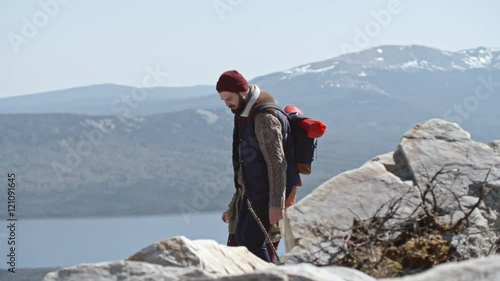 Handheld tracking shot of young stylish couple walking hand in hand on rocky terrain high up in mountains during romantic hiking trip photo