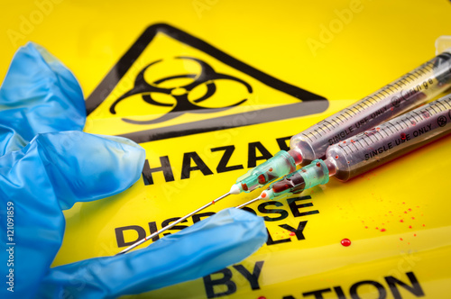 Blood filled syringes and blue medical gloves on yellow biohazard bag and spilled biological waste