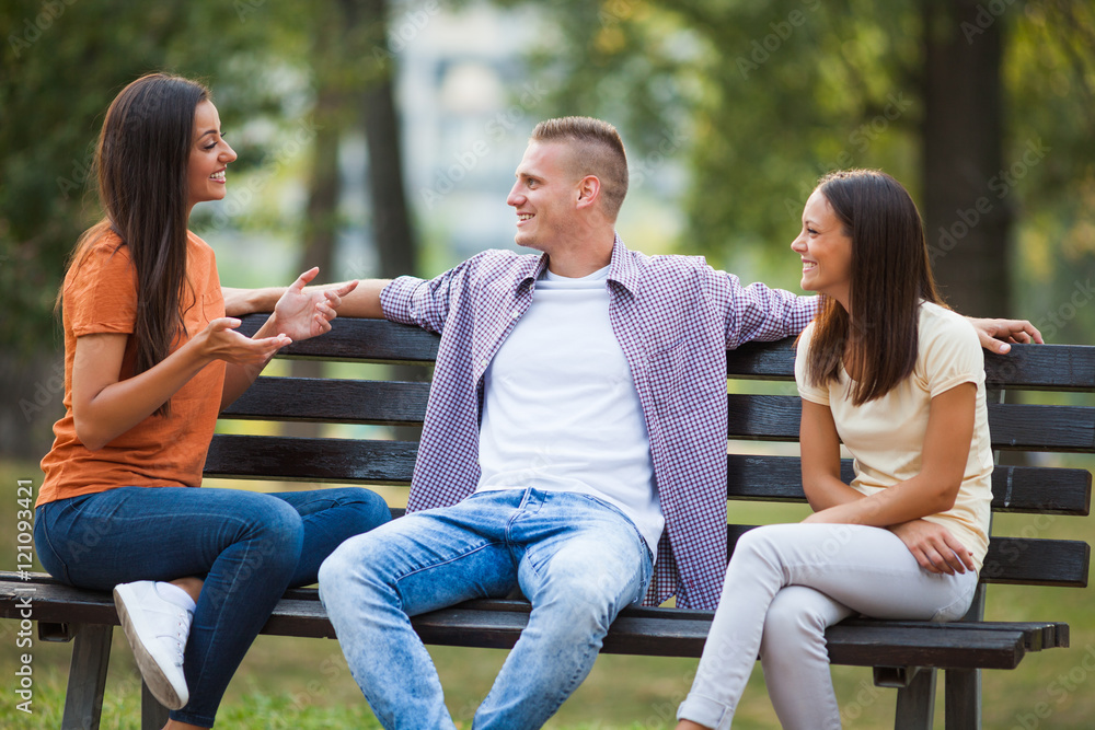 Three friends are sitting on bench in park and talking. Stock Photo | Adobe  Stock