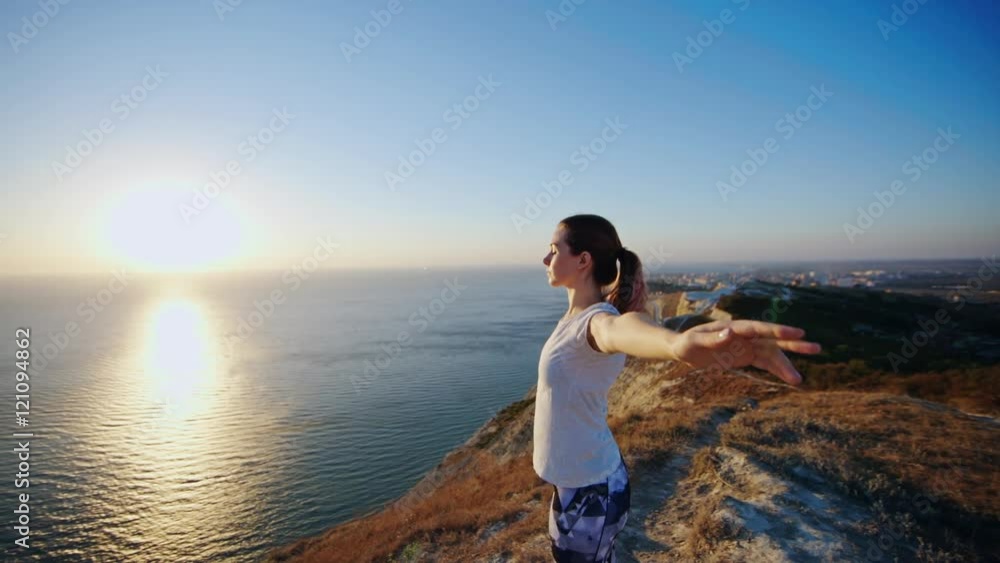 Girl standing on the cliff and raising her hands up. Аthletic beautiful woman enjoying a sunset or sunrise Girl standing on the cliff and raising her hands up. Аthletic beautiful woman enjoying a sunset or sunrise