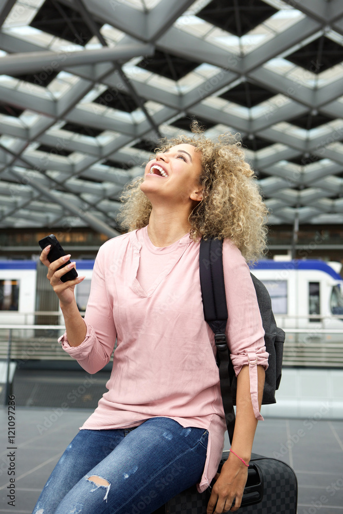 Laughing traveler sitting on suitcase with cellphone Laughing traveler sitting on suitcase with cellphone