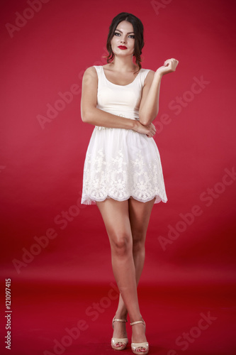 Young beautiful female model in white dress on red background