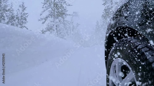 Winter. Road in the forest and lots of snow. The front tire of the car and heavy snowfall