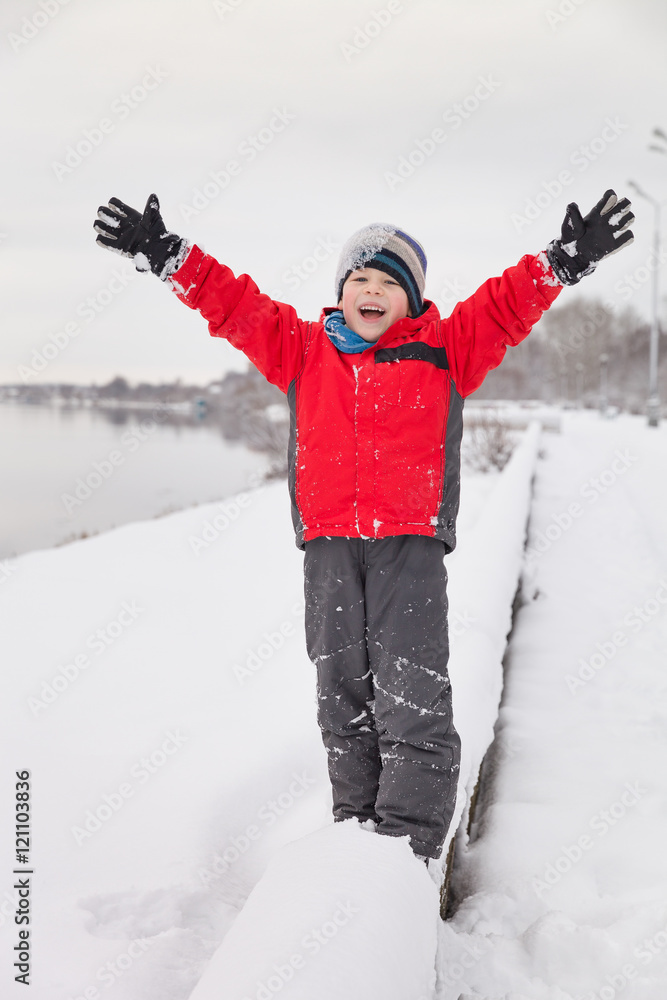 Portarit of cute preschool kid boy playing with snow and having fun in the park. Child with hands up on a cold winter day outdoors.