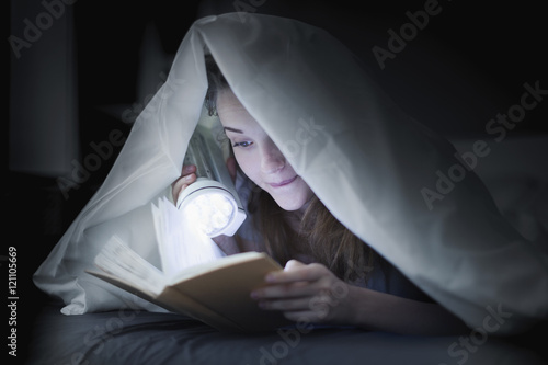 Teenage girl reading a book in bed under the covers