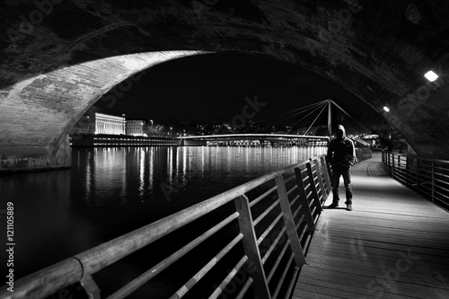 Man with hoody standing in a threatening pose in a tunnel under a bridge at night.