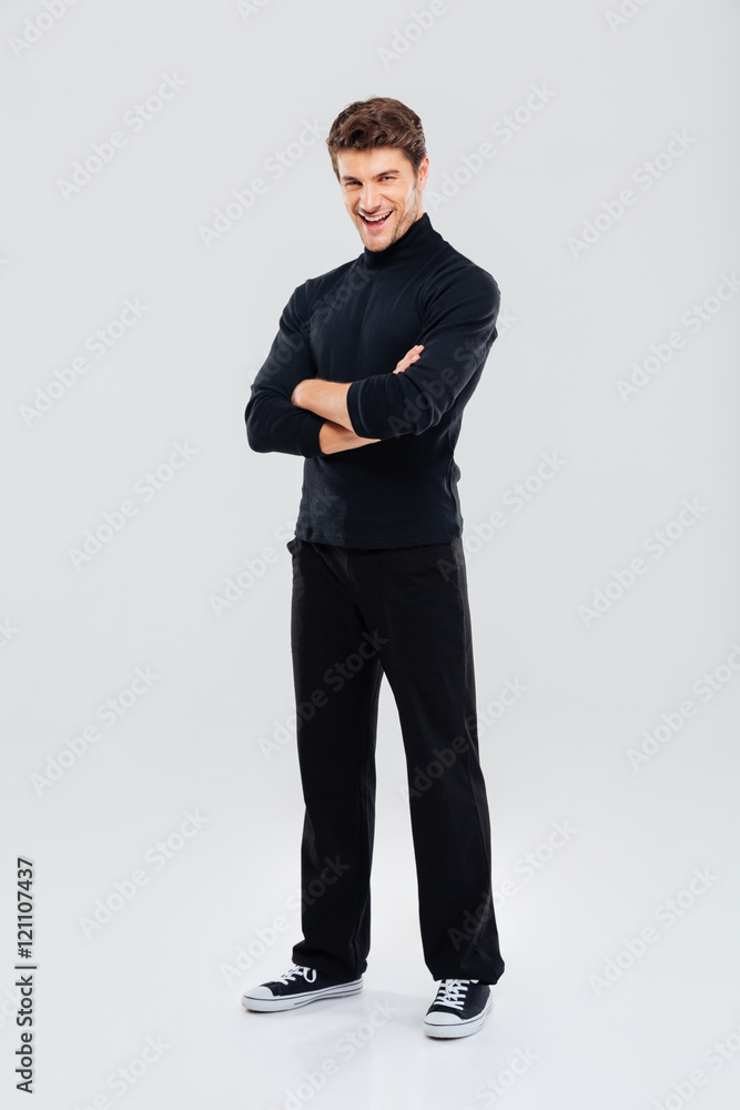 Handsome young man standing with arms crossed and laughing