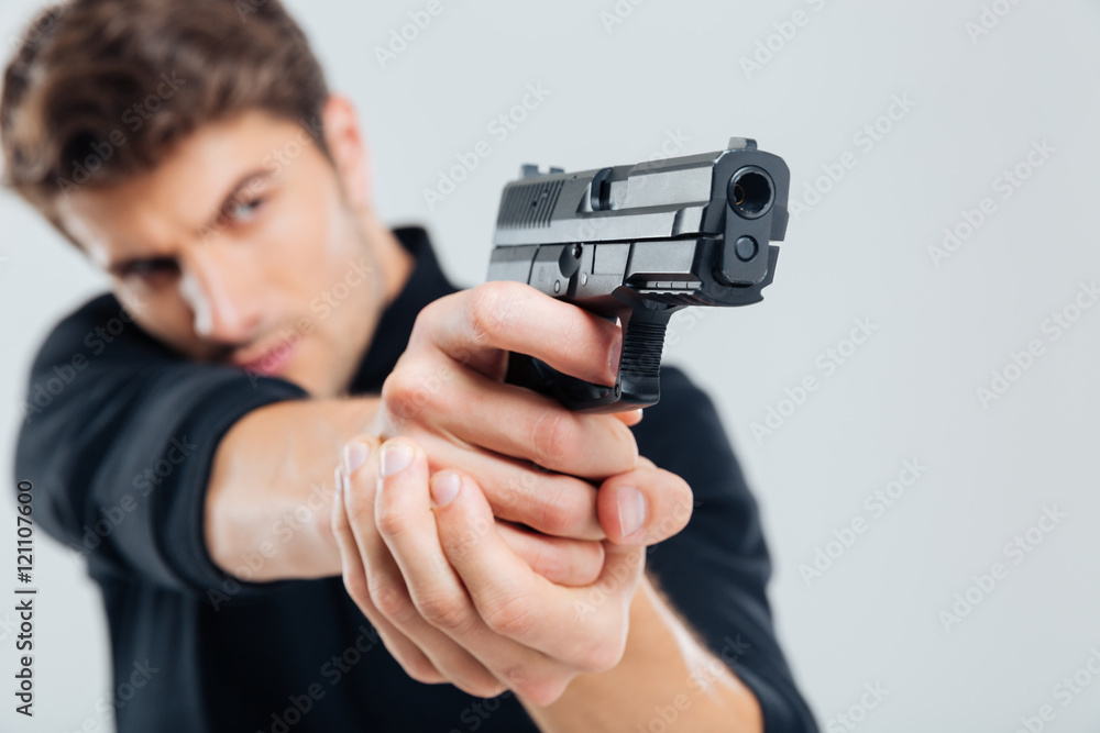 Serious young man standing and aiming with gun Serious young man standing and aiming with gun