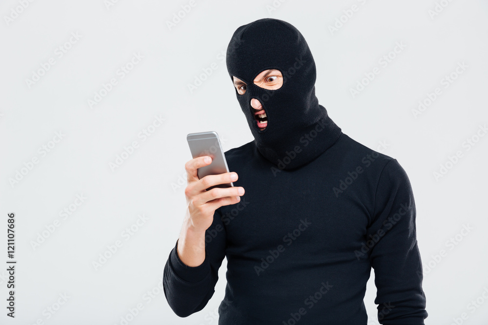 Angry young man in balaclava using cell phone Angry young man in balaclava using cell phone